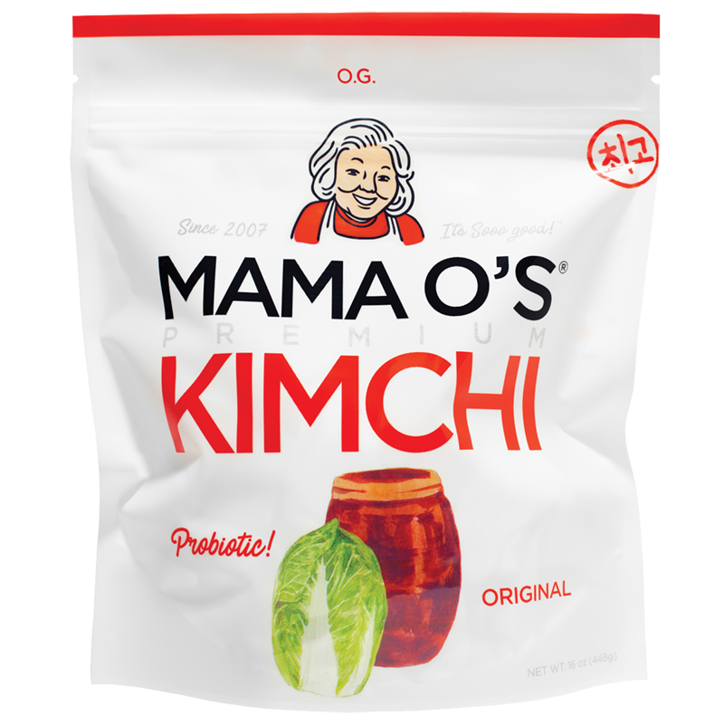 A white package of Mama O’s Premium Kimchi featuring a cartoon woman’s face, bold red text “KIMCHI,” an image of a jar and napa cabbage, and labels for “Probiotic!” and “Original.”.