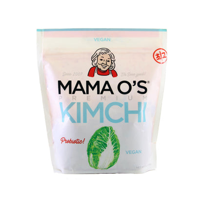 A white pouch of Mama O’s Premium Vegan Kimchi, featuring a smiling woman and napa cabbage on the front with a “Probiotic!” label, showcases the probiotic benefits in every bite.