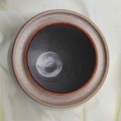 Top view of a custom handmade Mama O’s Homemade Kimchi Kit bowl by Mama O’s Premium Kimchi, featuring a dark matte interior and speckled beige rim, placed on light fabric.